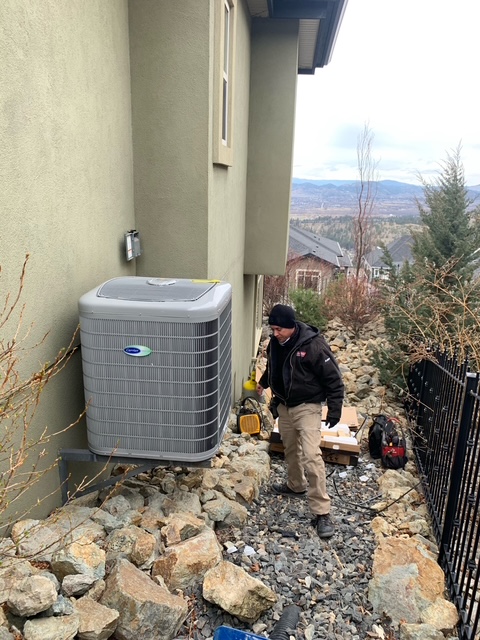Quality Air Care technician servicing an outdoor air conditioning condenser at an Okanagan home