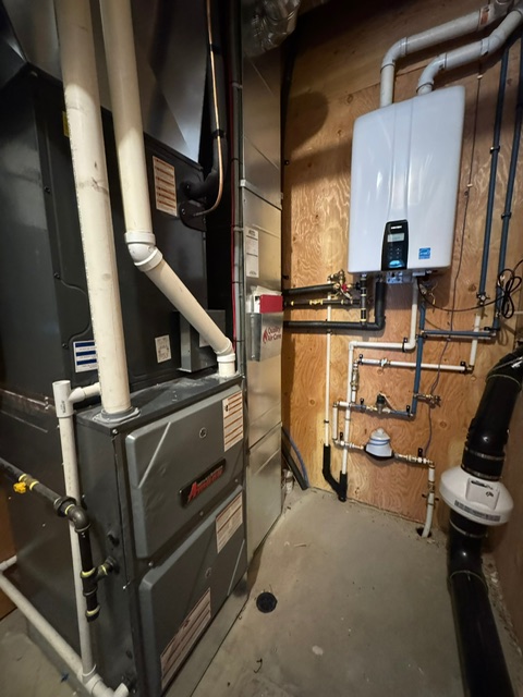 Wall mounted tankless water heater piped beside a gas furnace